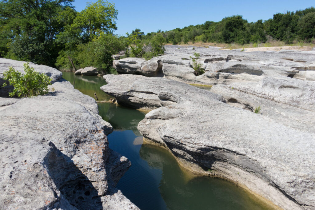 A creek carved through limestone rock and flows towards trees in the distance