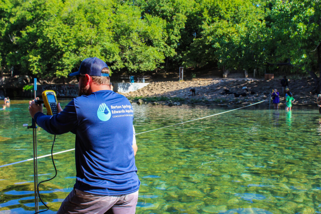 District staff measuring barton springs flow by standing in the water with equipment near Barking Springs