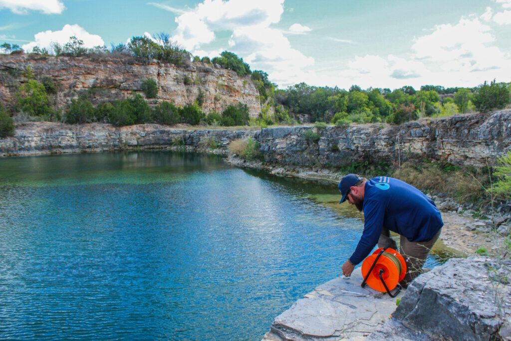 BSEAD staff lean over a cliff to measure a lake that's fed by the Edwards Aquifer.