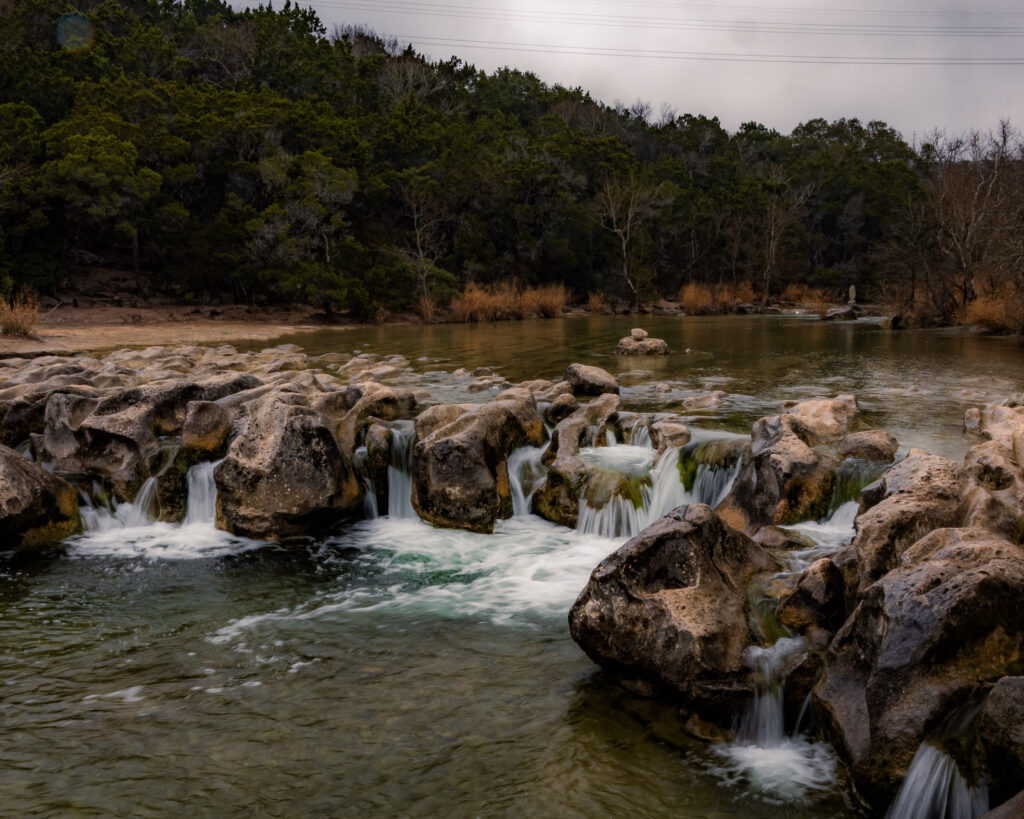 Water from Barton creek falls over a waterfall at Sculpture Falls on a cloudy day in Austin, TX